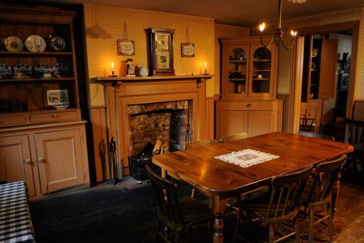 Photo of a dining room interior, including a wooden table with six chairs, a fireplace, and two china cabinets containing glasswear.