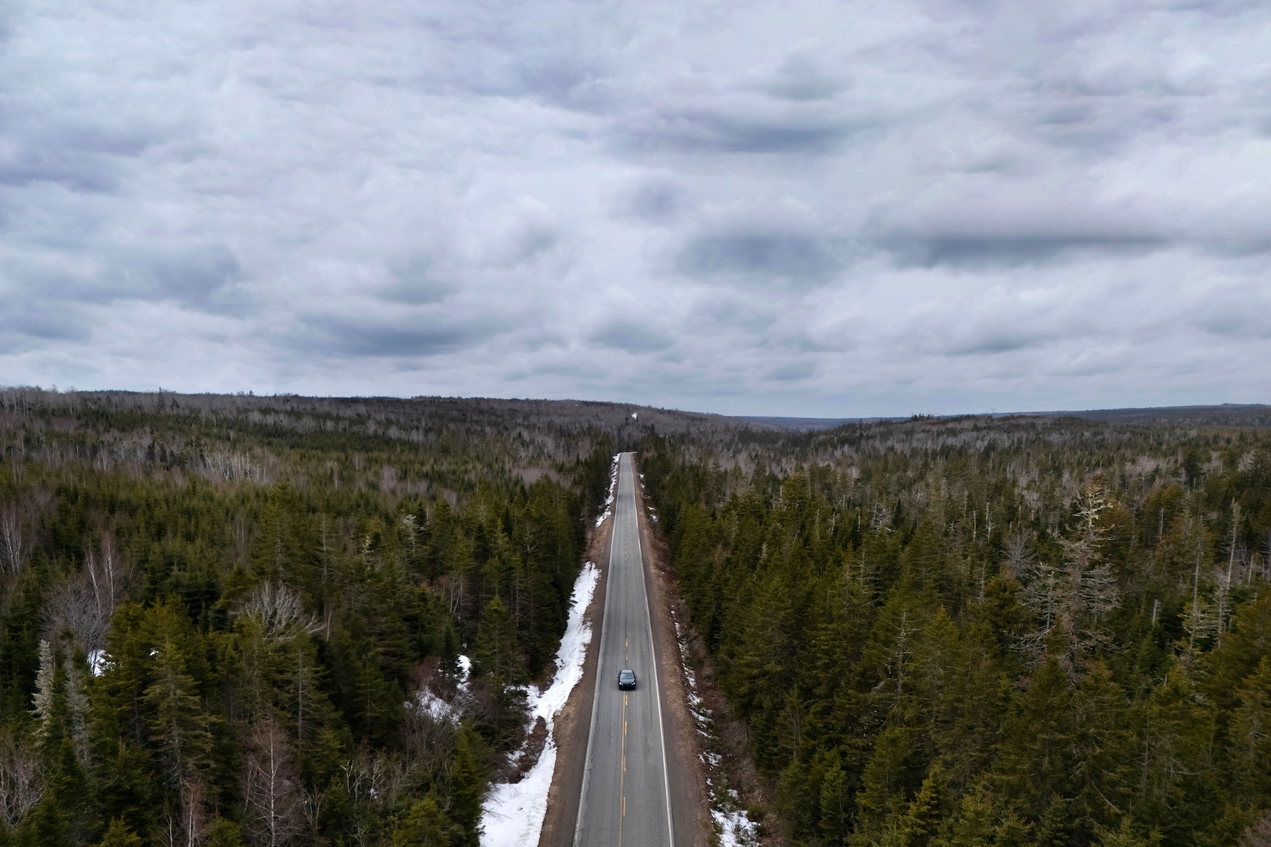 Photo of a highway road surrounded by coniferous forest with a cloudy sky above.