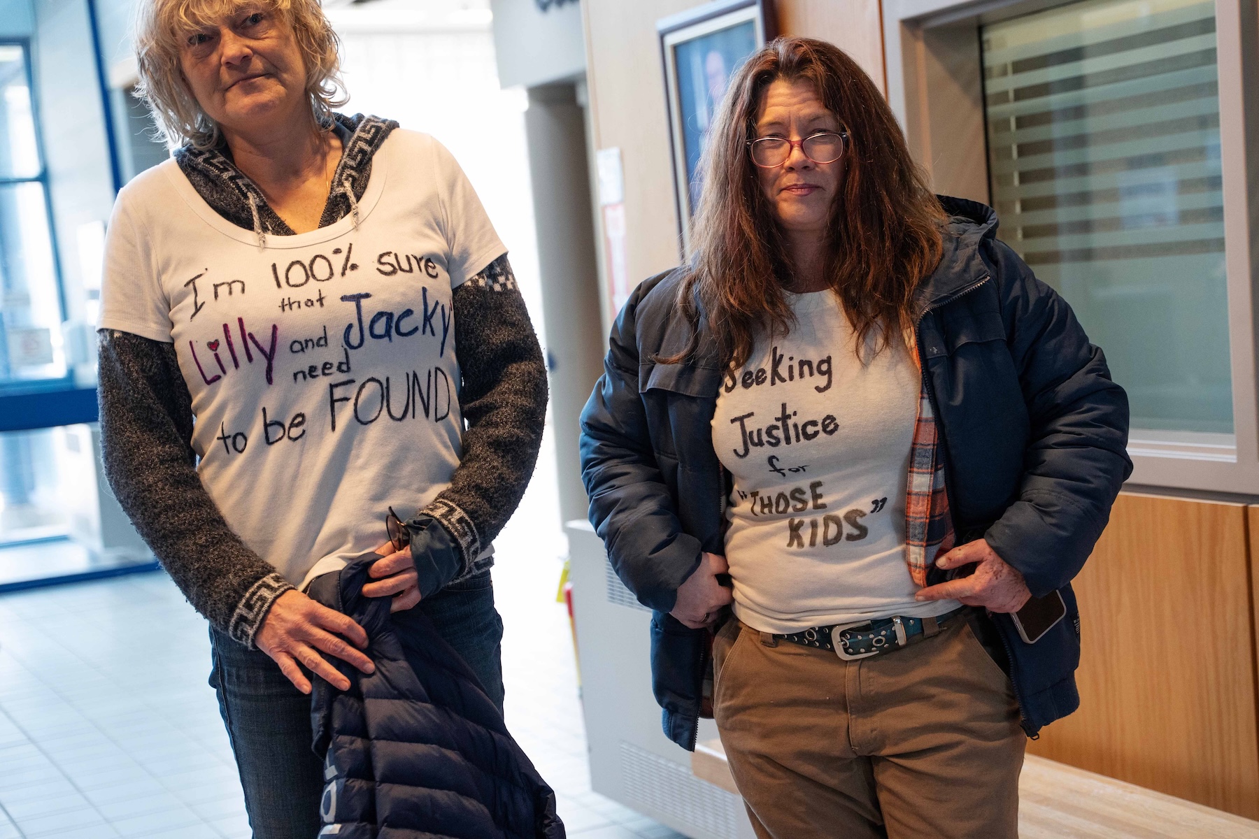 Photo of two women, one with short grey hair and the other with long brown hair, wearing white, homemade T-shirts which read 'I'm 100% sure that Lilly and Jacky need to be found,' and 'Seeking justice for those kids'.