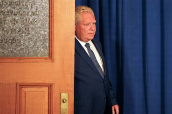 Photo of Doug Ford partially behind a door and walking into a room.