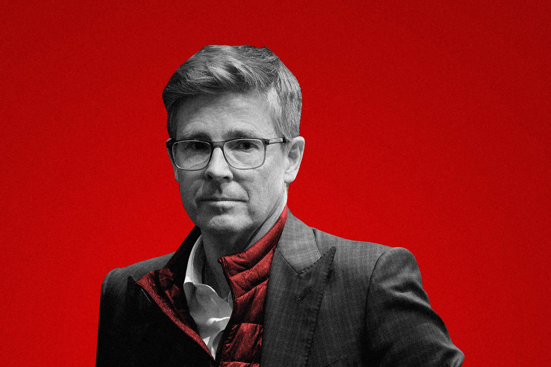 A black-and-white photo of Galen Weston Jr. wearing a red vest against a red backdrop.