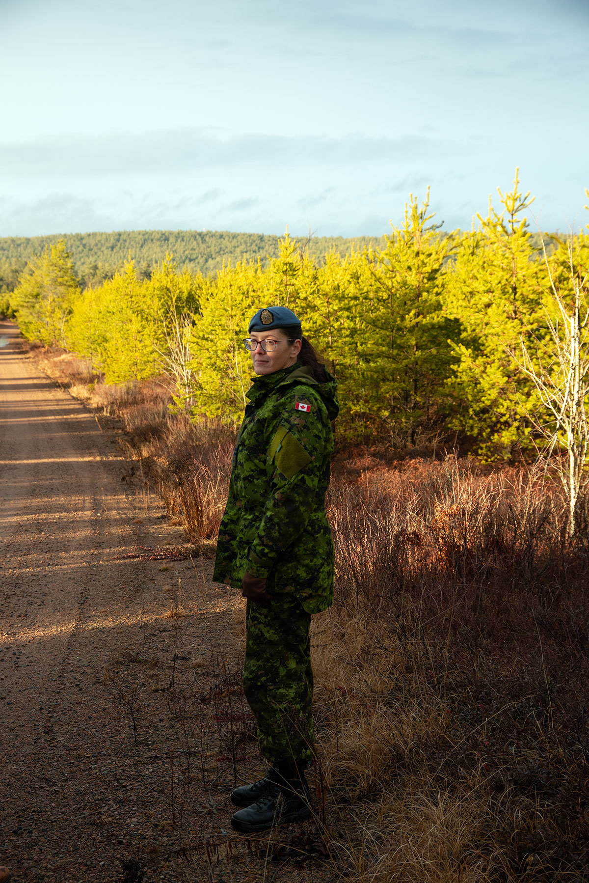 Photo of Captain Pam Turney, wearing green camo and a beret, in a stand of jack pine at CFB Petawawa
