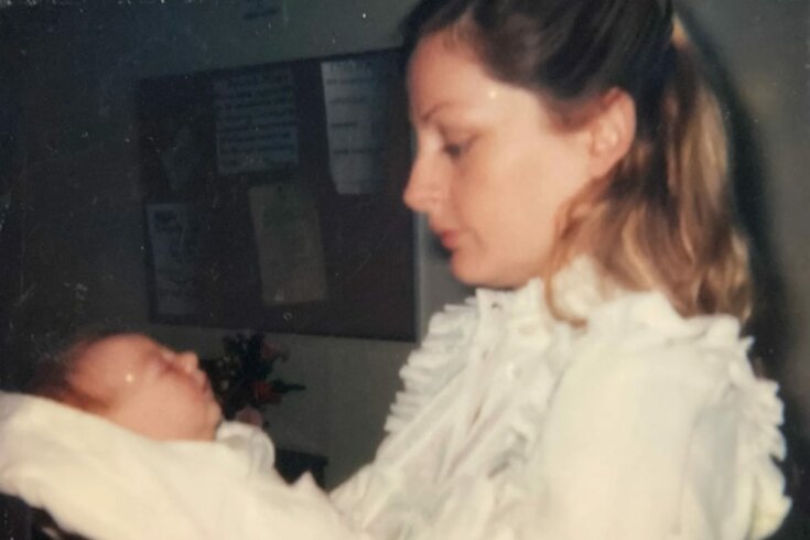 A photo of a mother wearing a white frilly top facing an infant swaddled in a white blanket.