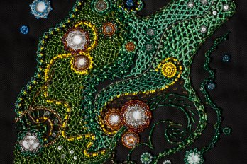 A celestial nebula composed of a latticework of green beads, with a line of yellow threaded throughout, and small circles outlined with brown and blue beads.