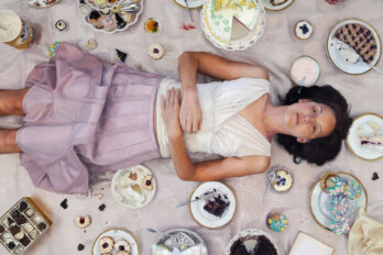 A woman lies on the ground surrounded by cakes and other sweets.