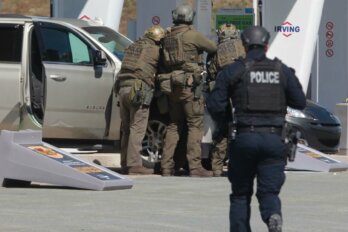 Photo shows a group of RCMP officers with their backs to the camera positioned outside a car at a gas station