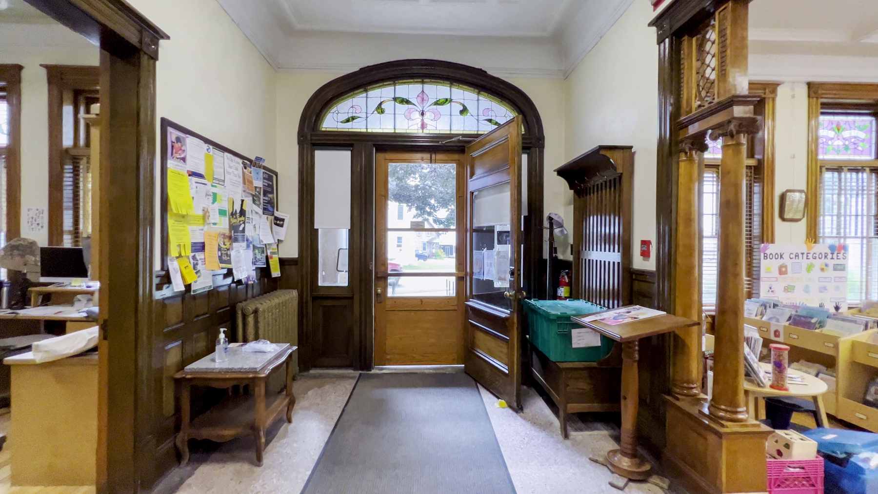 A photo of a library entryway. The wooden-frame door is open. Above it are small, stained glass windows.
