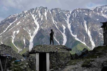 A soldier stands on guard at a post against the backdrop of snow-covered mountains