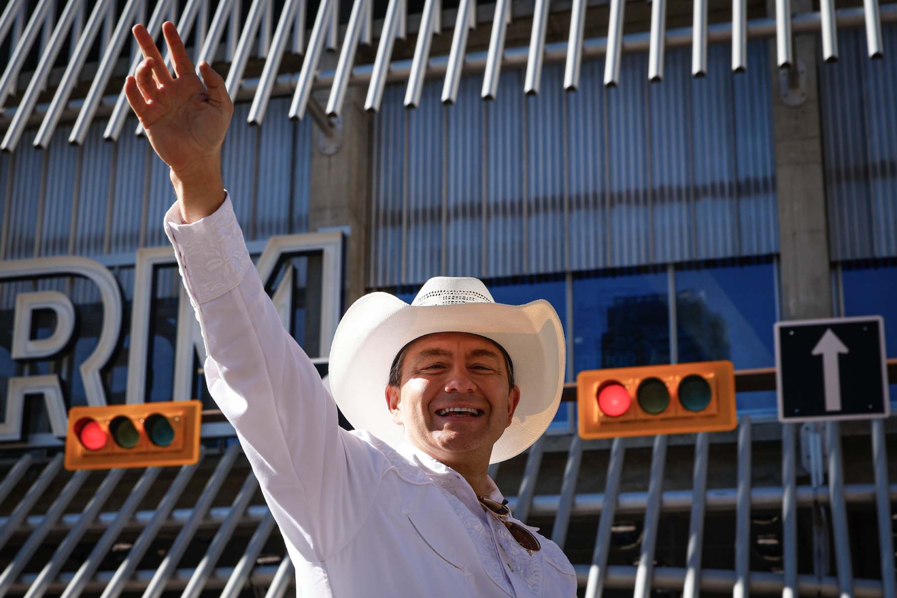 Photo of Pierre Poilievre in a white shirt and white cowboy hat with his hand extended to wave.
