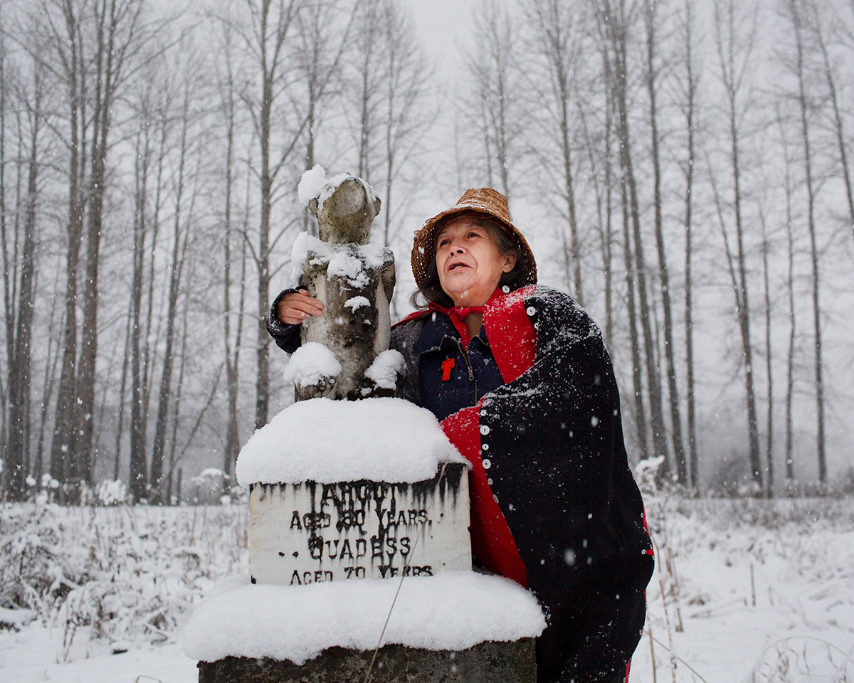 Photo of Rosaline Starr Gawa 2Auntys, wearing traditional clothing, standing in a snowy forest by the grave of one of her ancestors.