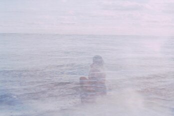 A multiple exposure 35mm film photograph showing a view of Toronto island beach, where a woman sits at the water's edge, looking over her shoulder.