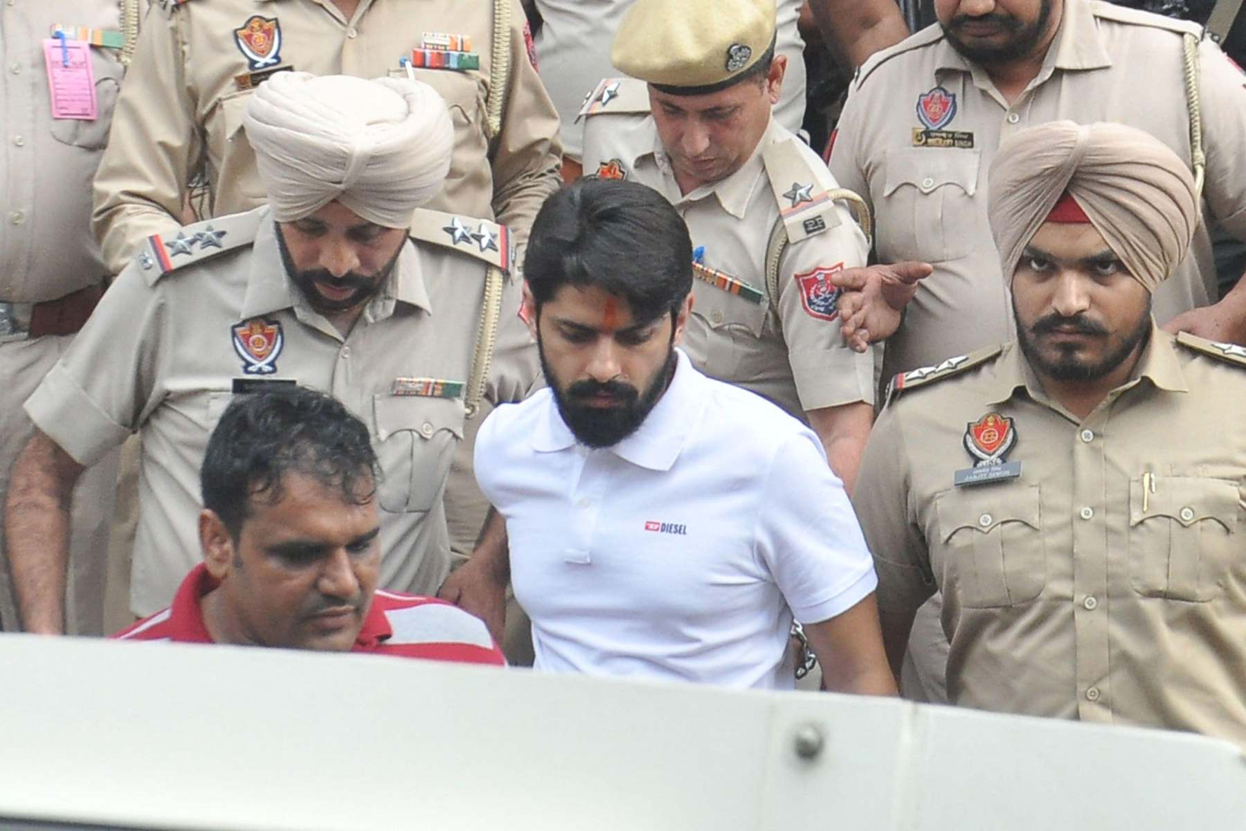 Photo of a man in a white shirt surrounded by policemen in khaki-coloured shirts.