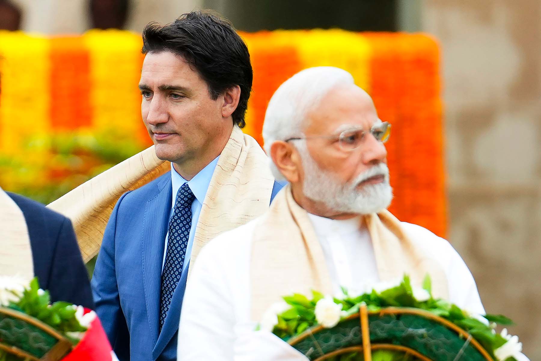 A closeup of Canadian Prime Minister Justin Trudeau facing away from Indian Prime Minister Narendra Modi at Raj Ghat, against a backdrop of yellow and orange decorations at Mahatma Gandhi's cremation site, during the G20 Summit in New Delhi in 2023.