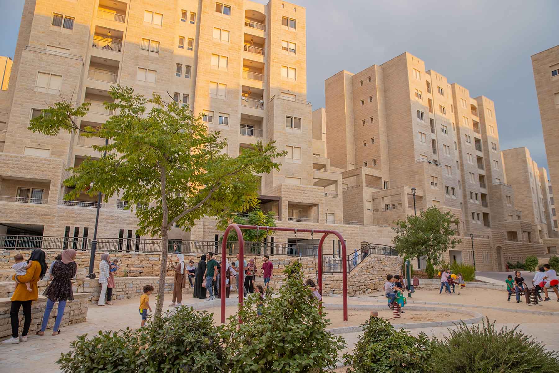Children and families congregate in a playground with mid-rise apartment buildings in the background