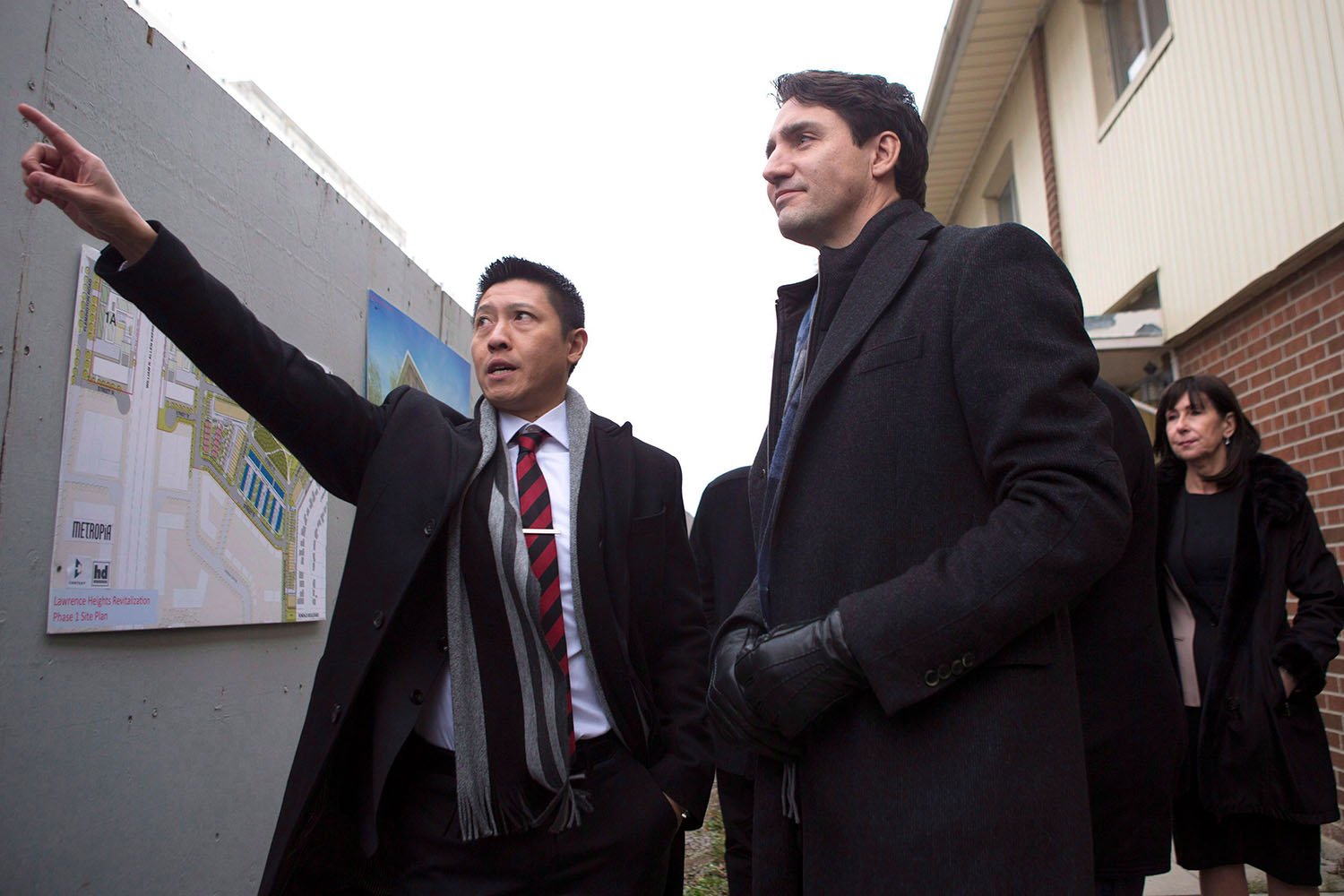 Justin Trudeau and Jason Chen visit a Toronto housing development. Chen points at something in the distance and Trudeau smiles beside him.