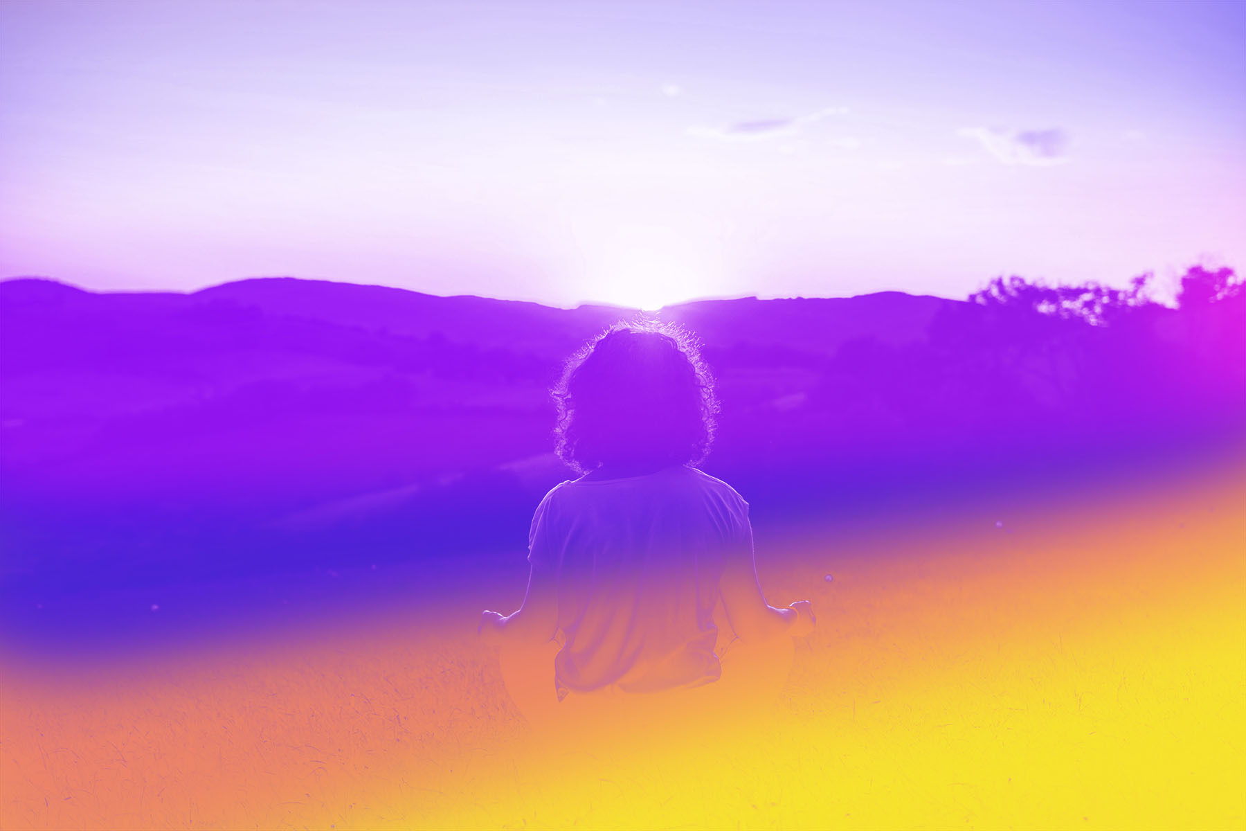 A person sitting in a meditation post looking at the sunrise.