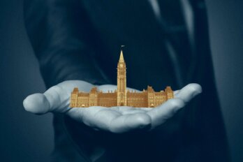 In a photo illustration, a blue-suited man holds a miniature, gold-coloured Parliament building in his hand