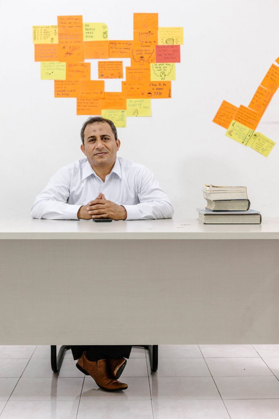 Mohamad Al-Radhi, sitting at desk with wall of sticky notes behind