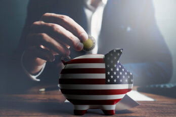 A photo illustration of a man in a suit putting a toonie into a piggy bank covered in the American flag