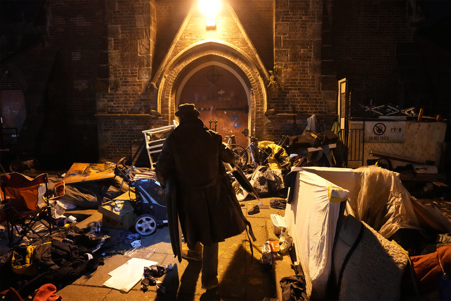 Photo shows the silhouette of a person in the night light amid objects scattered at an encampment