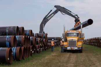 Crane loading up giant pipe onto a yellow tractor trailer