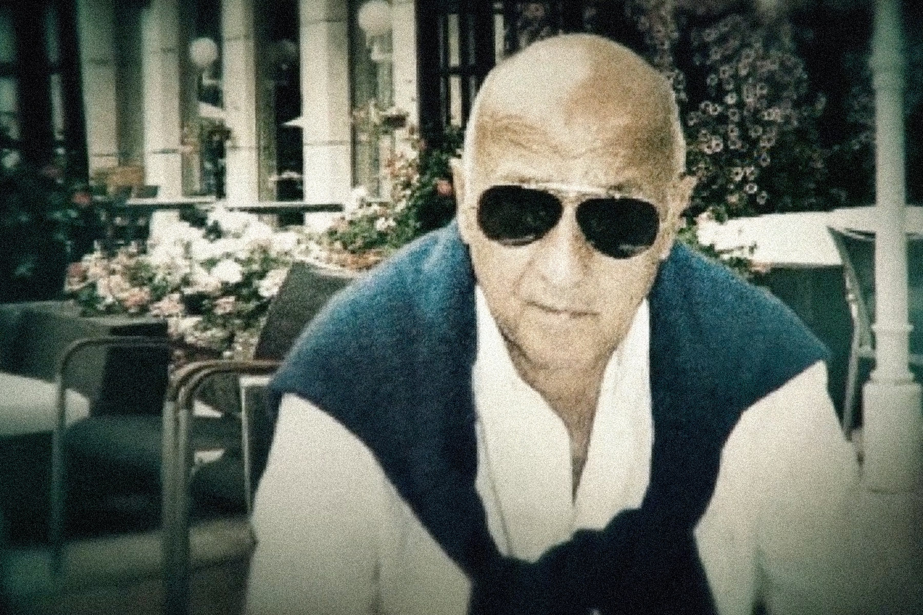Image of an old man wearing dark sunglasses staring at the camera.