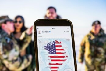 Photo of an image of Greenland containing an American flag displayed on a phone screen with soldiers in the background.