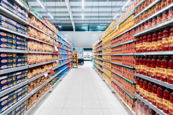 Photo looking down a supermarket aisle with fully stocked shelves.