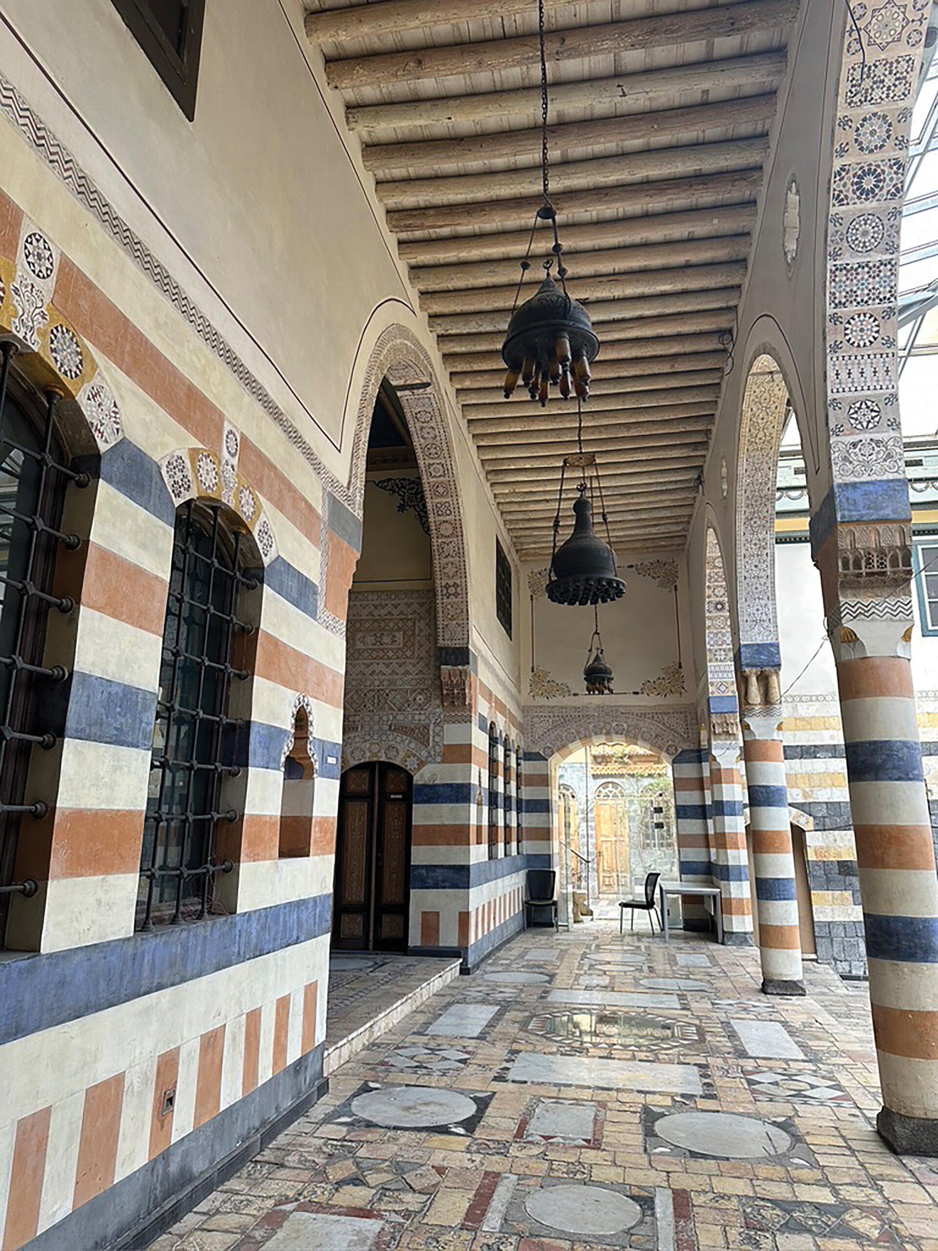 A photo of the exterior of a building with arched doorways and faded blue, red and white tiles arranged in stripes