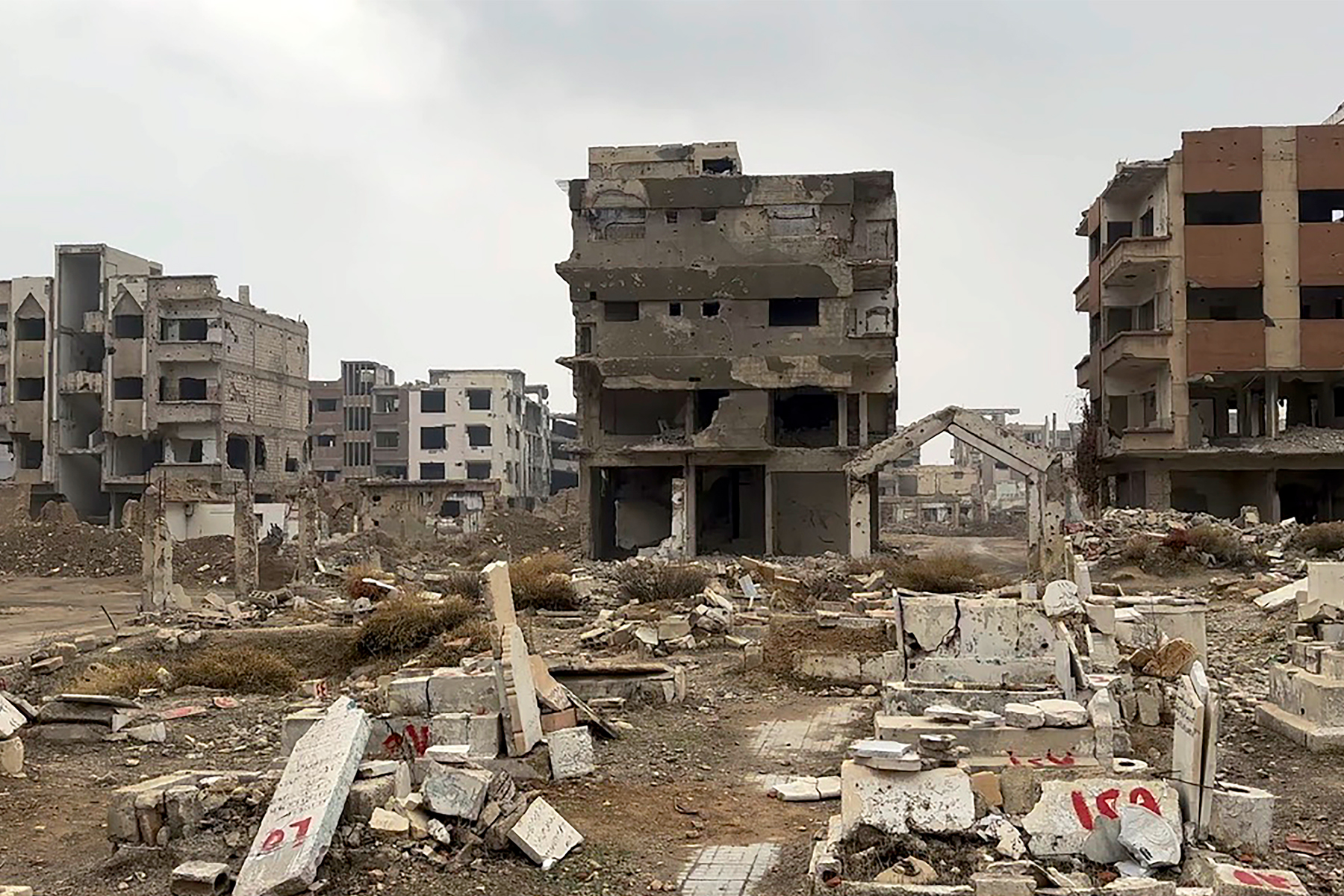 A photograph of several mid-rise buildings that are mostly shells with visible damage. Debris lies on the ground