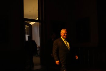 Ontario Premier Doug Ford walks to his office; there is a bit of light streaming in between the otherwise dark corridor