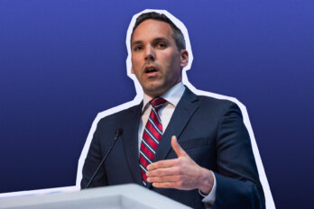 Photo of Yukon Premier Currie Dixon, a man with short dark hair wearing a suit and striped tie, speaking behind a podium on a blue background.