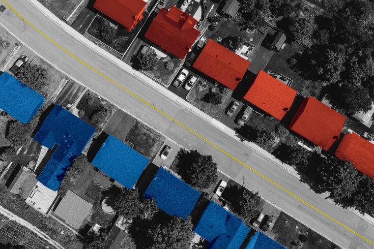 Aerial image of a residential street. One side of the street has houses with red roofs while the other side has houses with blue roofs.