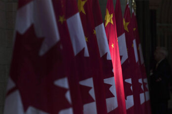 A photo of a Chinese flag illuminated by sunshine between Canadian flags in the Hall of Honour on Parliament Hill in Ottawa.