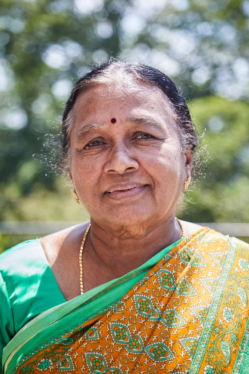 An older woman in a green and orange wrap smiles into the camera.
