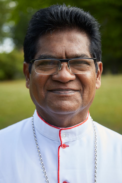 A closeup photo of Sampathawaduge Maxwell Grenville Silva, Auxiliary Bishop of Colombo, who is smiling into the camera.