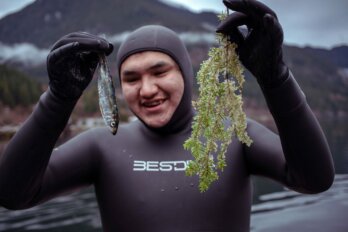 A man in a wetsuit holds a herring and hemlock sprig