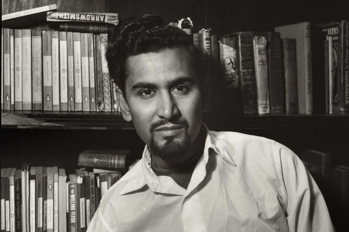 A black-and-white headshot of writer Samuel Selvon sitting in front of a bookcase.