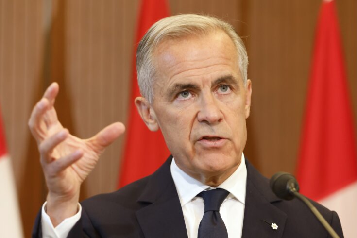 Photo of Prime Minister Mark Carney speaking on a stage in front of hanging Canadian flags.