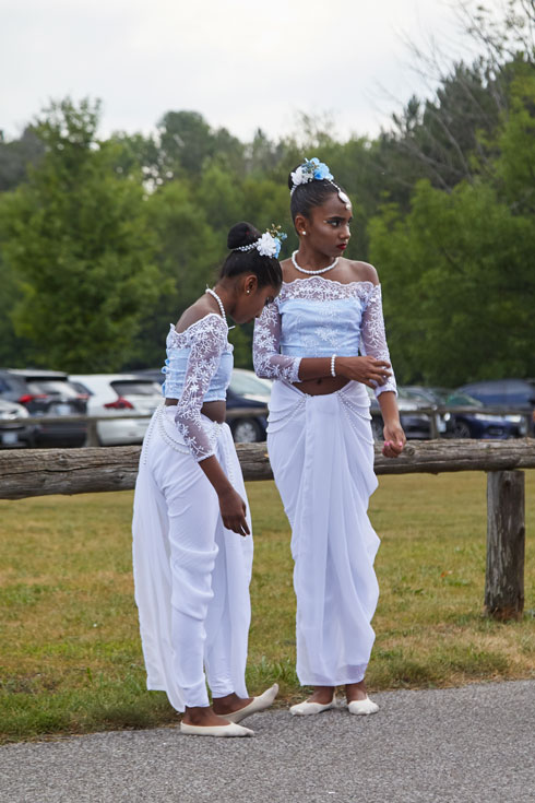 Two young dancers in long white dresses, with lace sleeves, stand waiting before the procession.
